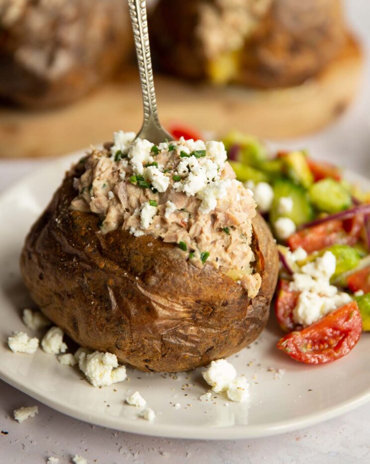tuna baked potato on white plate with silver fork digging in next to side salad
