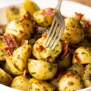 close up shot of silver fork digging into potato in large white bowl