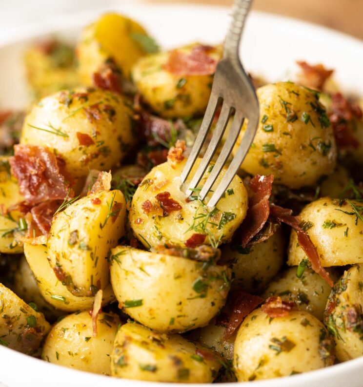 close up shot of silver fork digging into potato in large white bowl