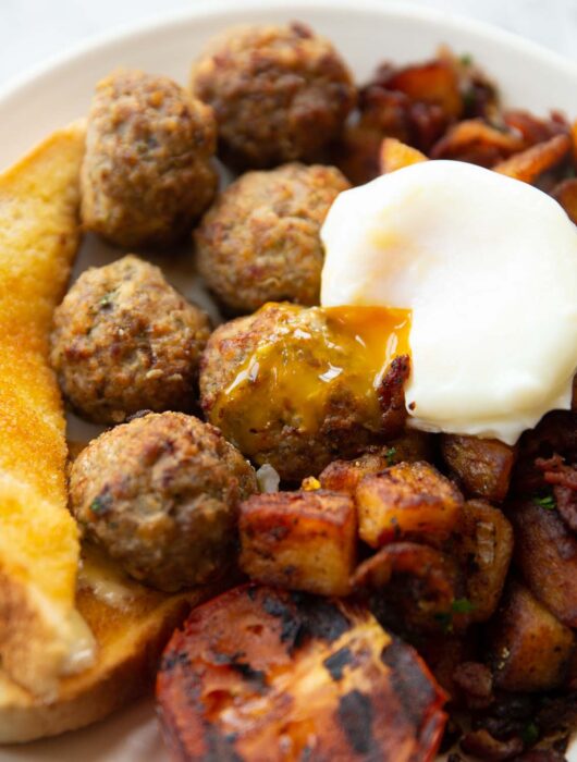 breakfast meatballs on white plate served with poached egg, toast tomato and potatoes
