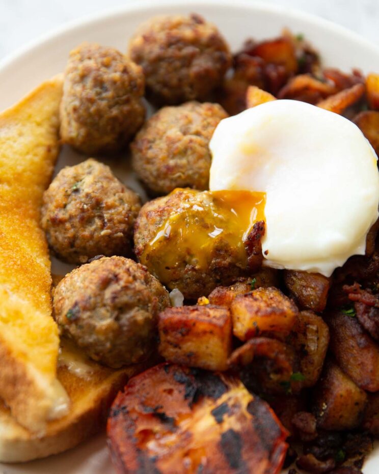 breakfast meatballs on white plate served with poached egg, toast tomato and potatoes
