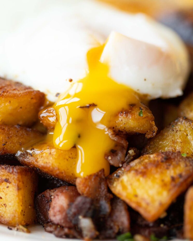 close up shot of poached egg yolk dripping down breakfast potatoes