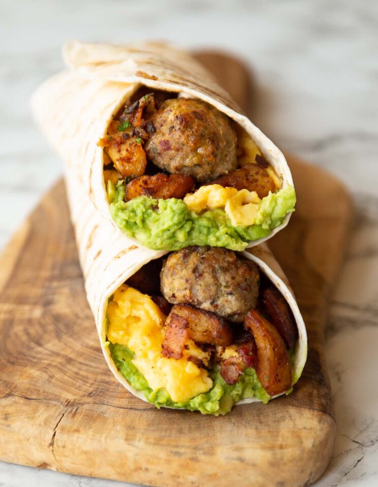 two breakfast wraps stacked on one another on wooden serving board