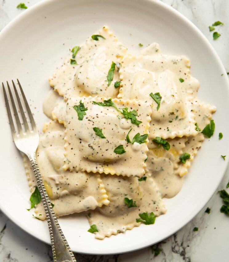 overhead shot of ravioli on small white plate with silver fork garnished with parsley