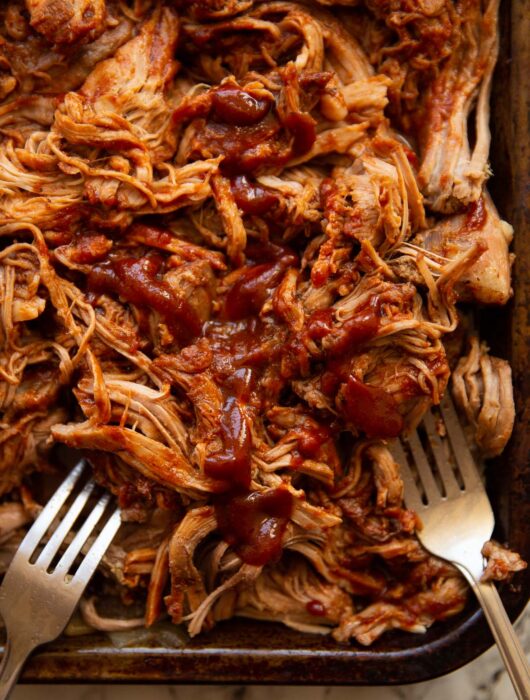 overhead close up shot of pulled pork on tray with two silver forks digging in