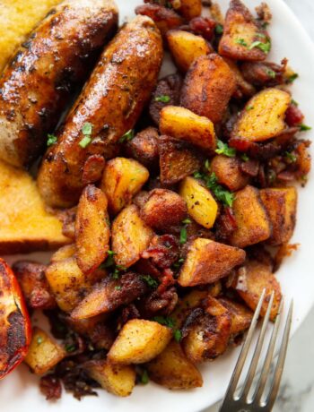 overhead shot of breakfast potatoes on white plate served with sausages, tomato and toast