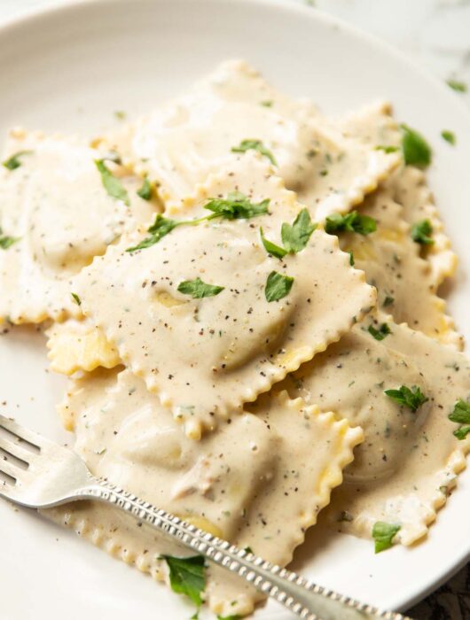 ravioli served on white plate garnished with parsley with silver fork