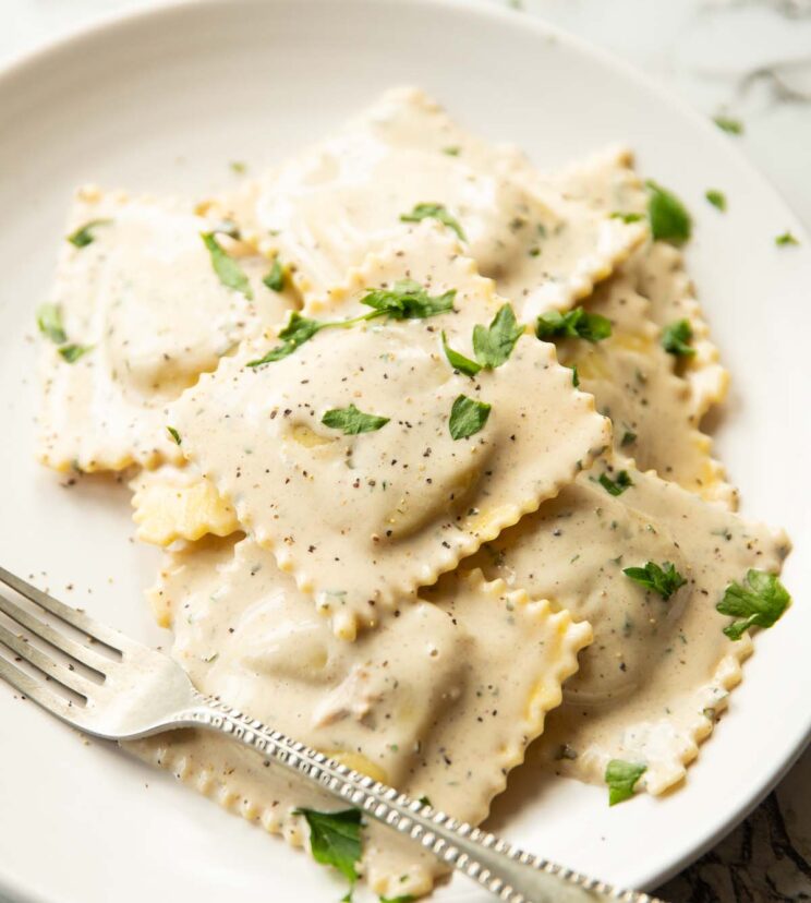 ravioli served on white plate garnished with parsley with silver fork