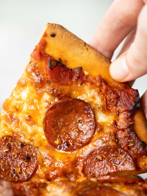 close up shot of hand lifting up slice of pepperoni pizza