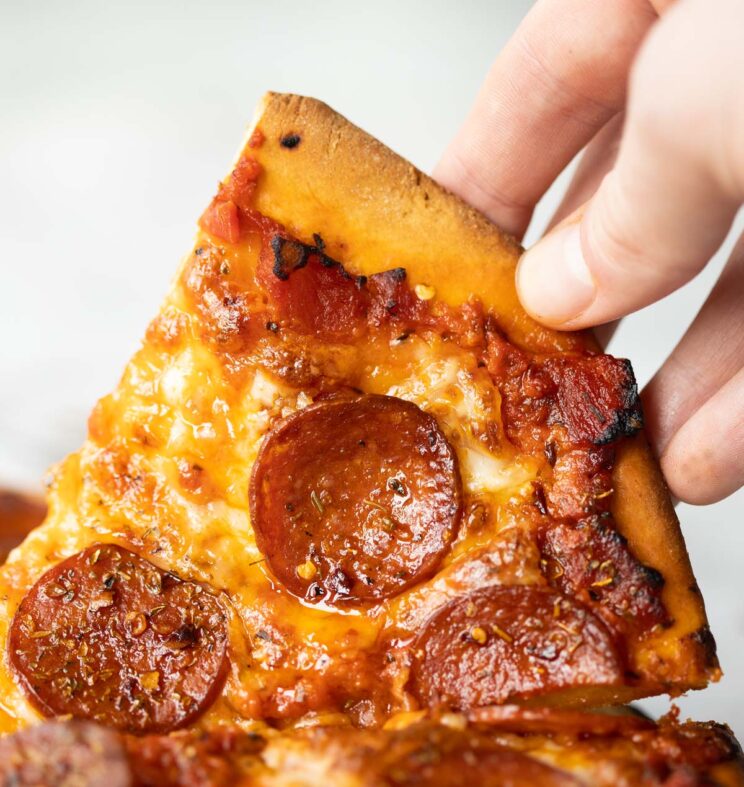 close up shot of hand lifting up slice of pepperoni pizza
