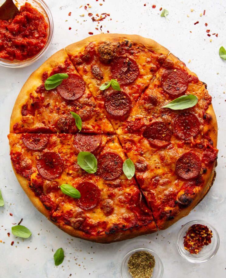 overhead shot of pizza sliced up on white background surrounded by chilli flakes and oregano