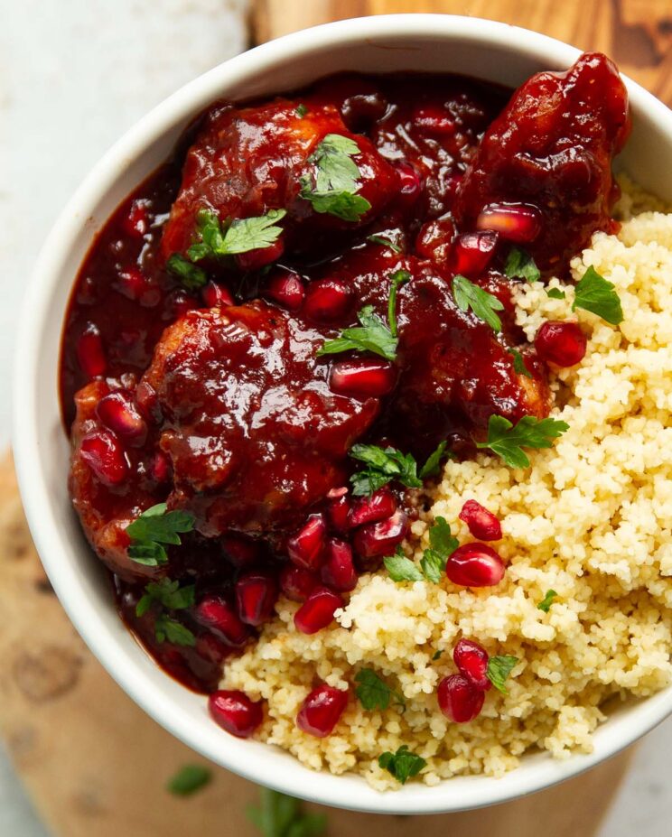 overhead shot of pomegranate chicken in small white bowl served with couscous