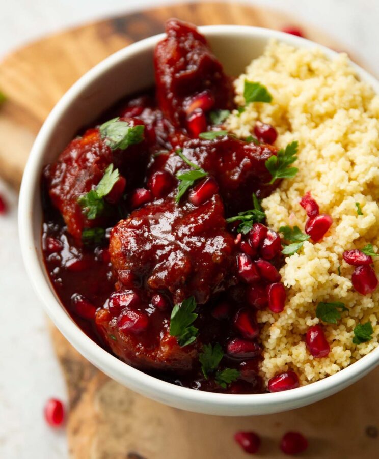 close up shot of pomegranate chicken in small white bowl on wooden board