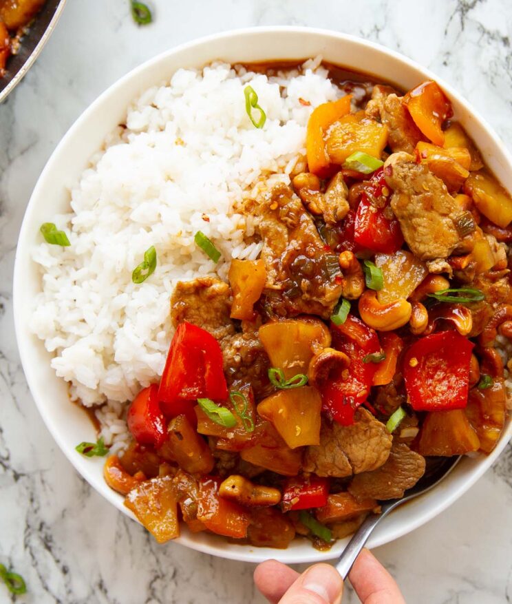 overhead shot of stir fry in big white bowl with rice and hand digging in with silver spoon