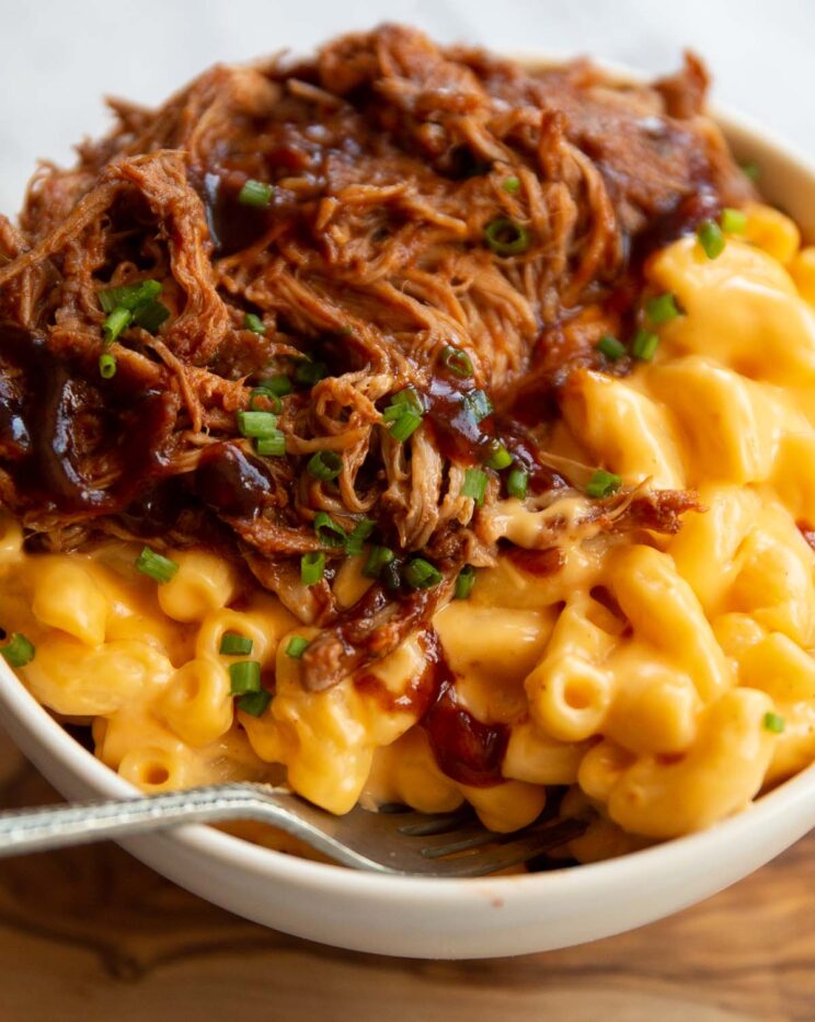 close up shot of pulled pork mac and cheese in small white bowl with silver fork digging in
