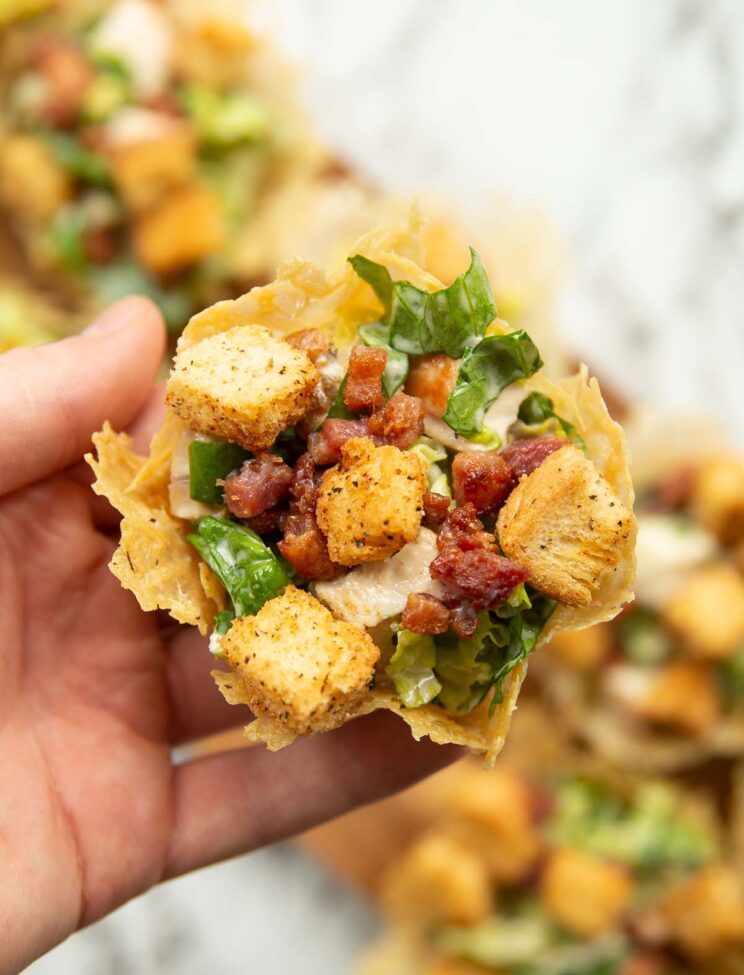 overhead shot of hand holding chicken caesar salad parmesan cups