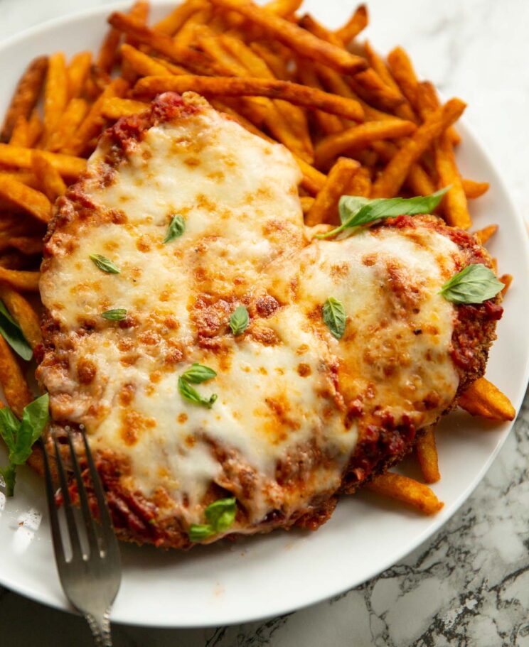 heart shaped chicken parmesan on white plate with fries