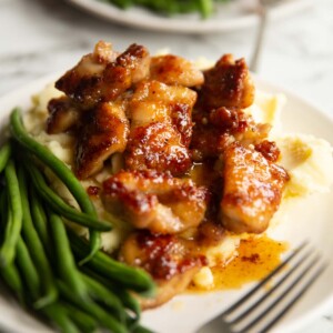 honey butter chicken on bed of mashed potato with green beans on small white plate