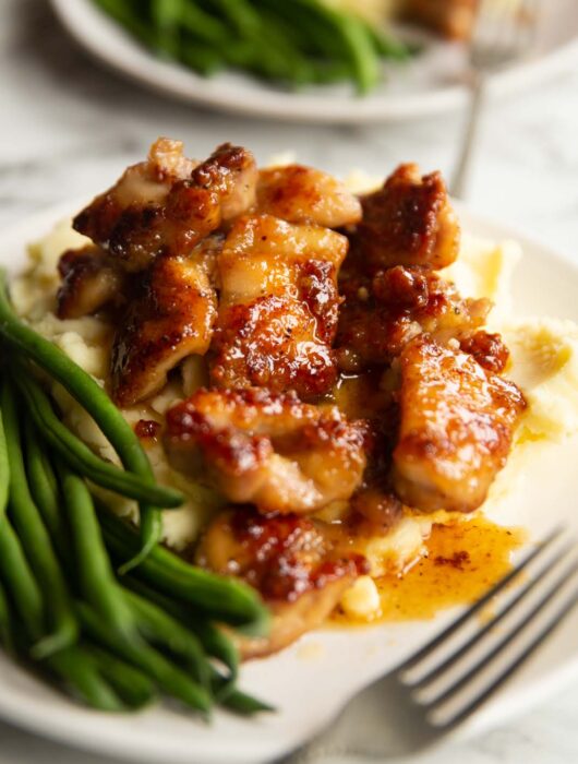 honey butter chicken on bed of mashed potato with green beans on small white plate