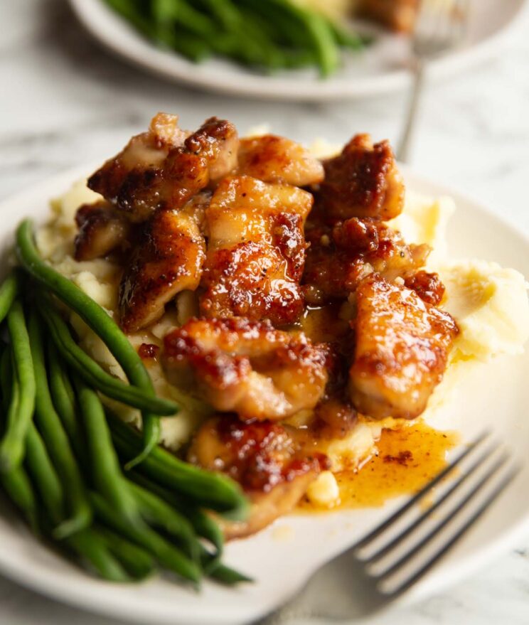 honey butter chicken on bed of mashed potato with green beans on small white plate