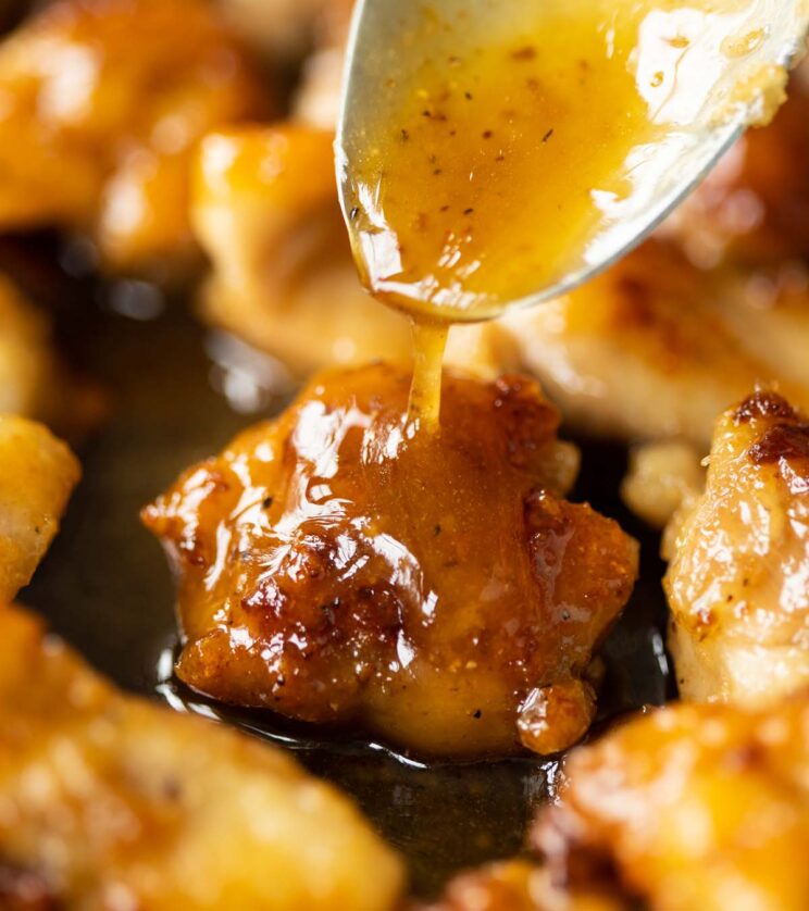 close up shot of silver spoon drizzling honey butter sauce over chicken in pan
