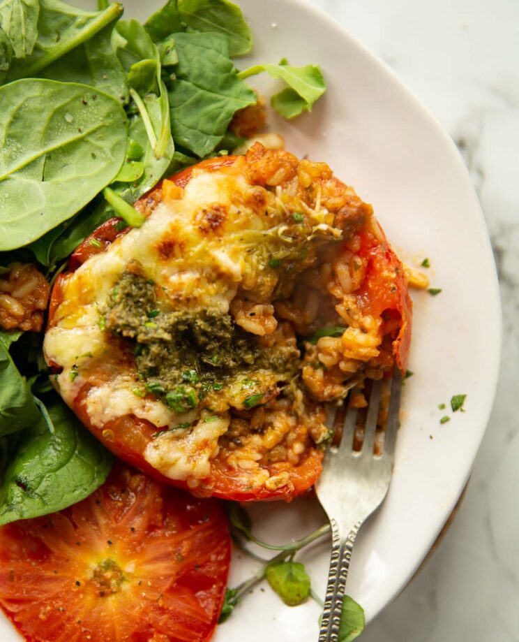 overhead shot of stuffed tomato on small white plate with spinach and fork