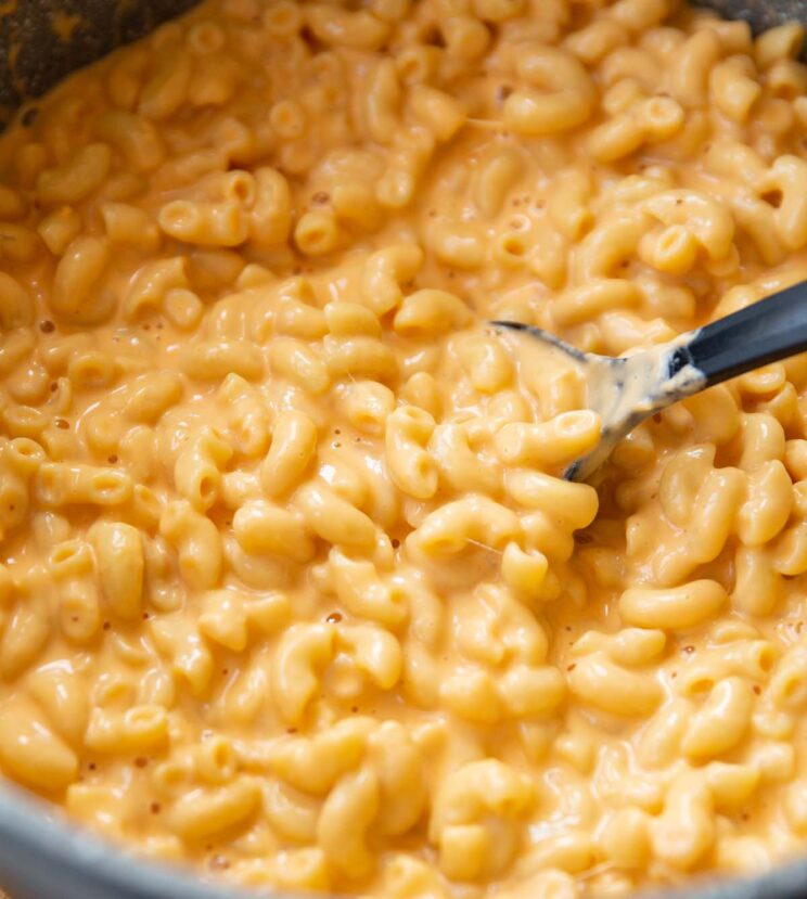 black serving spoon digging into large pot of mac and cheese