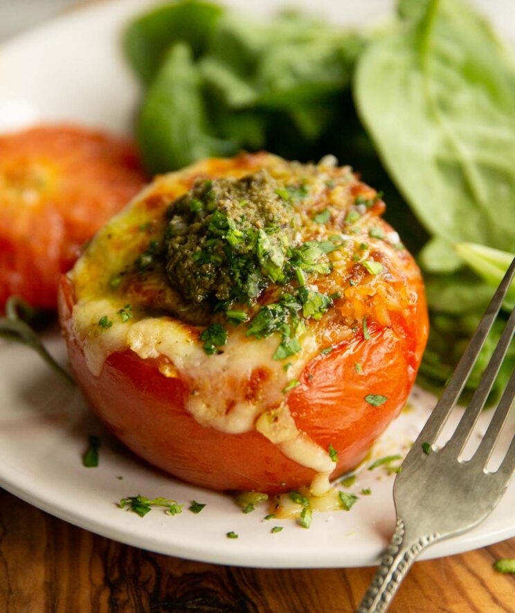 one stuffed tomato on small white plate with spinach in the background