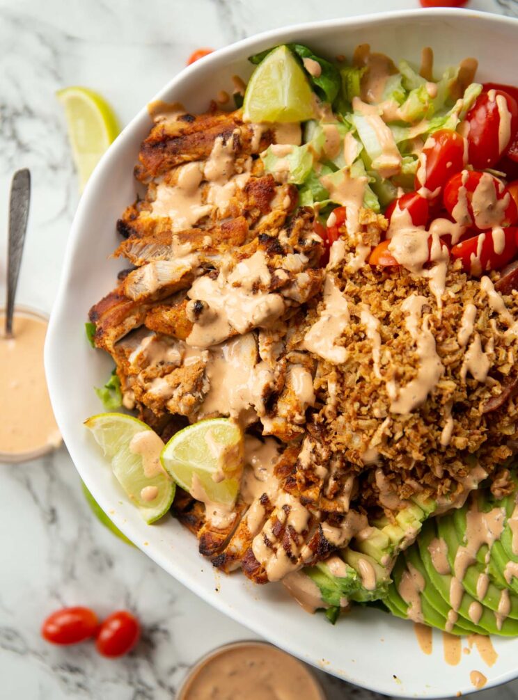 overhead close up shot of half of grilled chicken salad in large white bowl