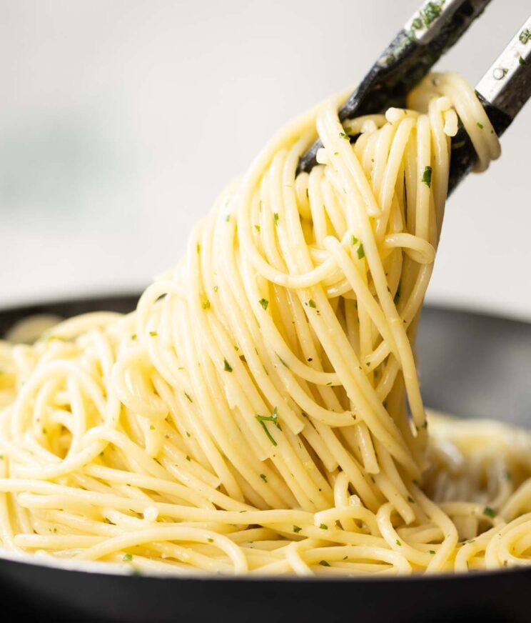 tongs lifting lemon pasta out of black frying pan