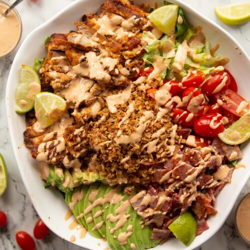overhead shot of grilled chicken salad in large white serving bowl on marble background