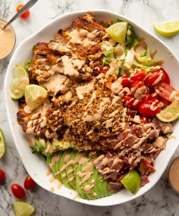 overhead shot of grilled chicken salad in large white serving bowl on marble background
