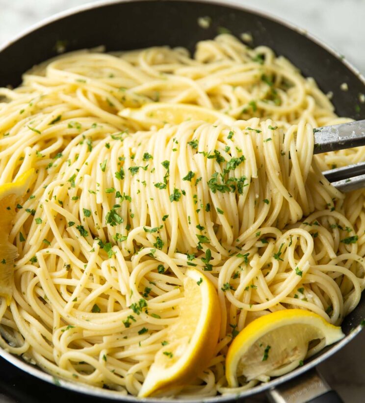 tongs twirling pasta in large black frying pan