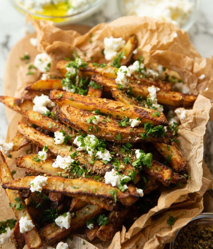 close up shot of fries in crumpled brown parchment paper garnished with feta and parsley