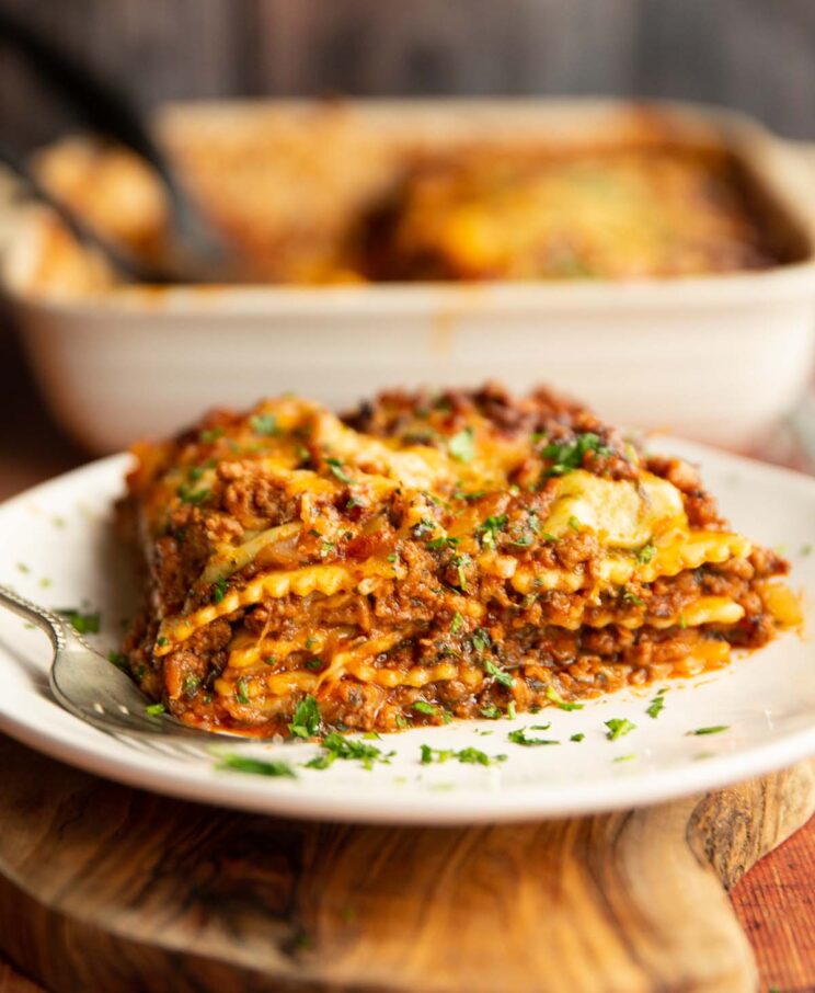 ravioli lasagne served on small white plate with silver fork garnished with parsley with dish blurred in background