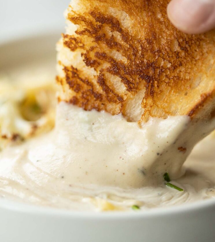 close up shot of dunking grilled cheese into small white bowl of cauliflower soup