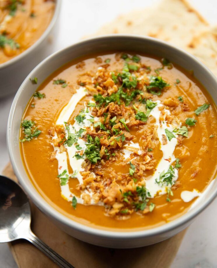 close up shot of curry sweet potato soup in large grey bowl garnished with fried onions, cream and coriander