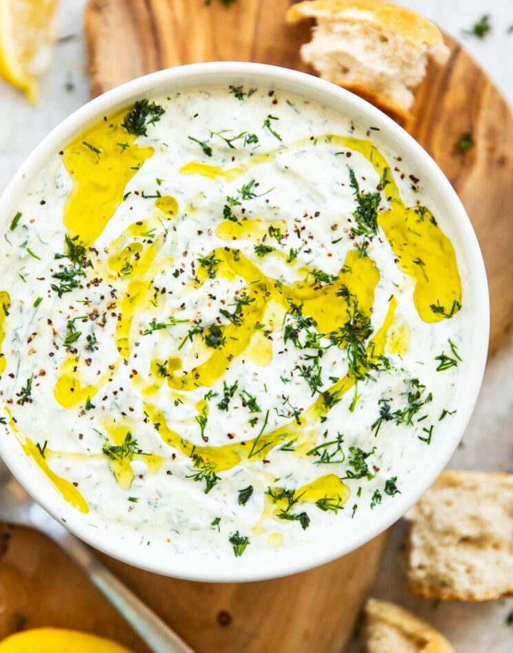 close up overhead shot of tzatziki in a white bowl on wooden board with bread and lemons