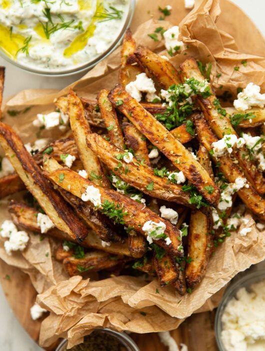 close up overhead shot of Greek fries in brown paper garnished with feta and parsley