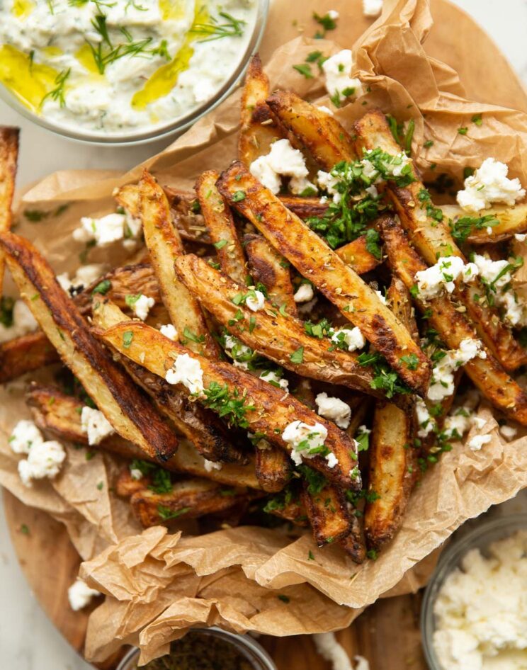 close up overhead shot of Greek fries in brown paper garnished with feta and parsley