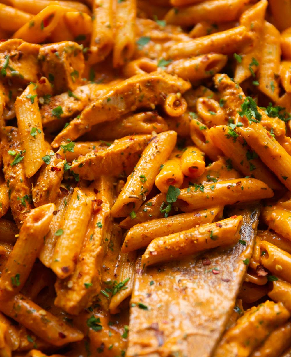 close up shot of peri peri chicken pasta in skillet with wooden spoon digging in