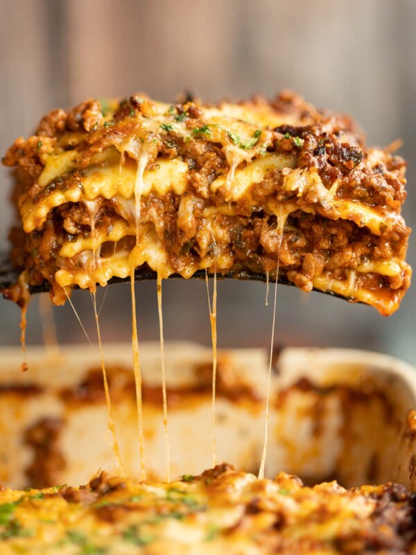 black spatula lifting ravioli lasagne from white baking dish