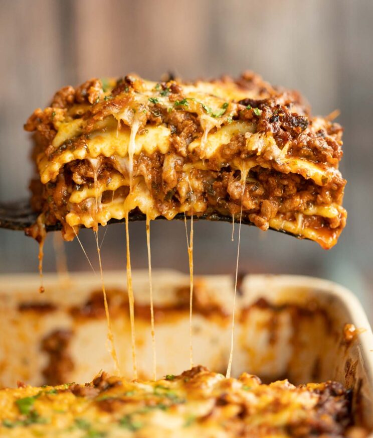 black spatula lifting ravioli lasagne from white baking dish