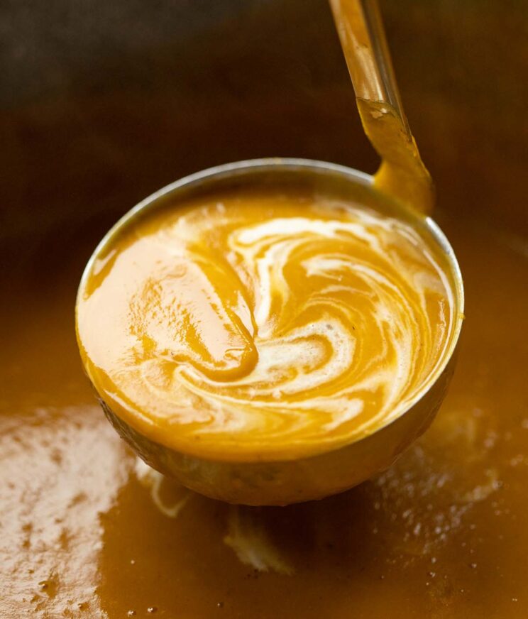 close up shot of ladle scooping up sweet potato soup from large pot