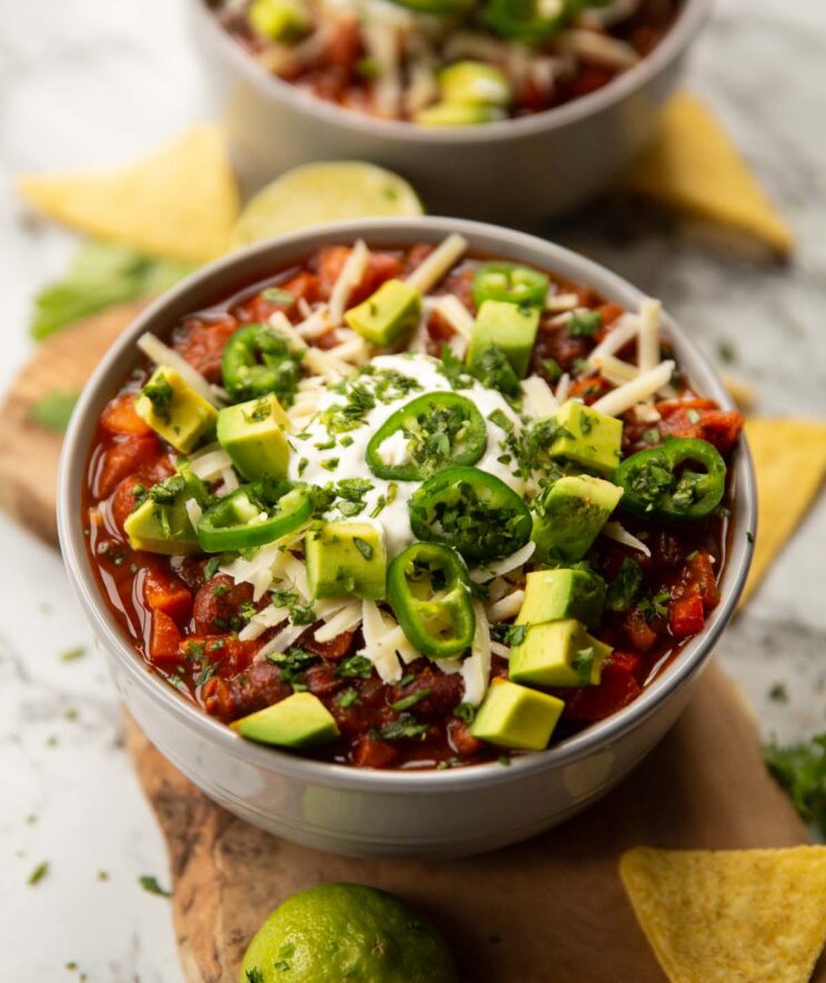 vegetable chilli served in grey bowl with toppings and second bowl blurred in background