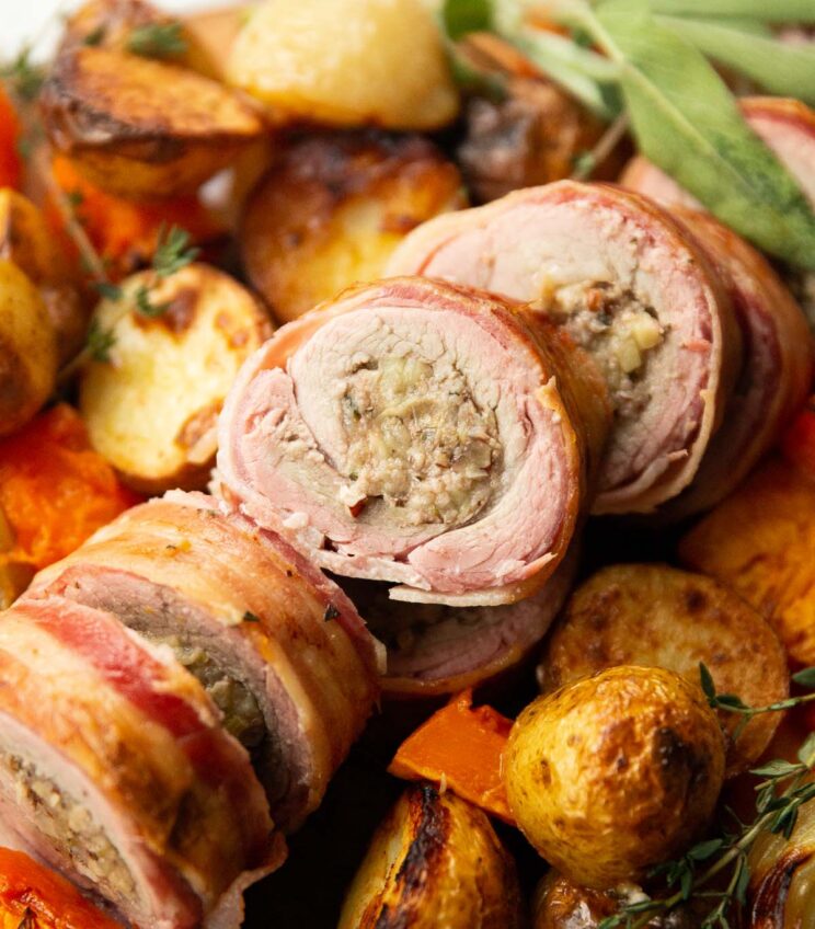 close up shot of sliced stuffed pork tenderloin on bed of roasted veg