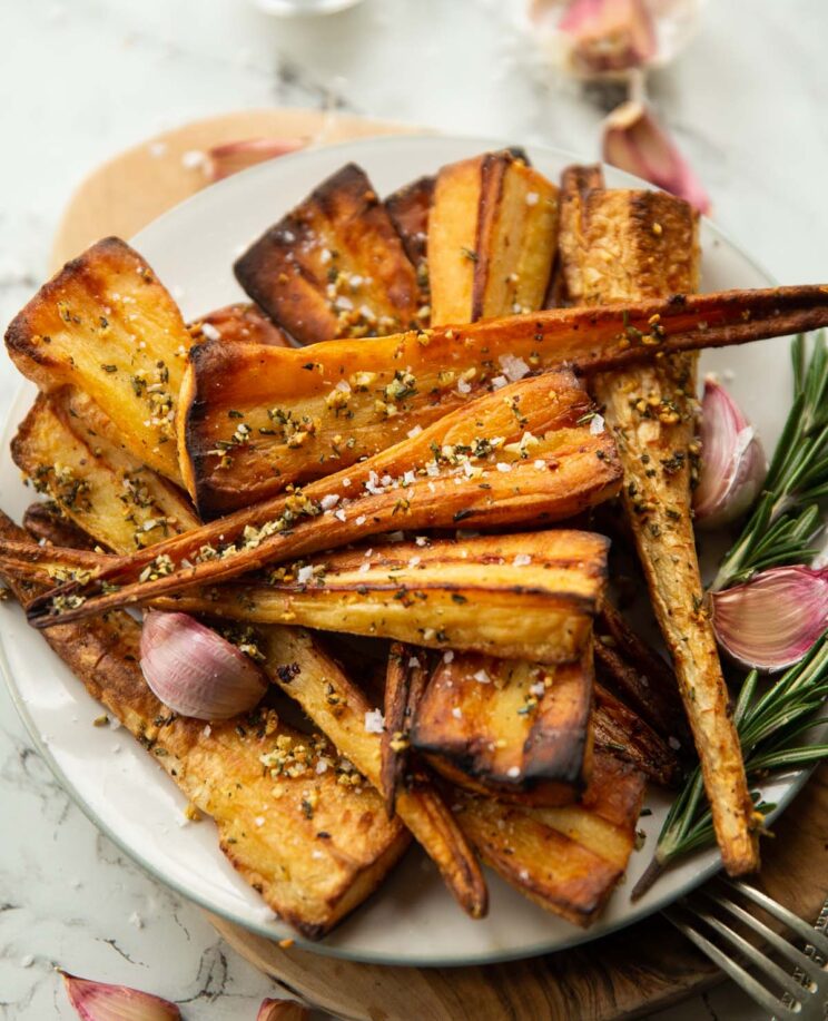 close up shot of roasted parsnips on small white plate with fresh garlic and rosemary