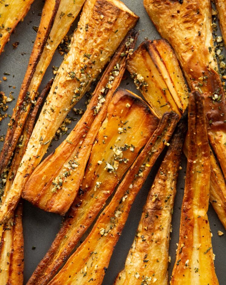 overhead shot of roasted parsnips fresh out the oven on grey baking tray