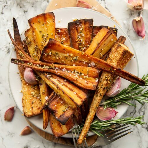 overhead shot of roasted parsnips served on small white plate garnished with fresh rosemary and garlic