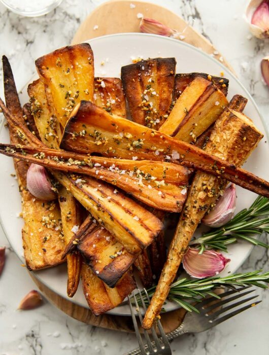 overhead shot of roasted parsnips served on small white plate garnished with fresh rosemary and garlic